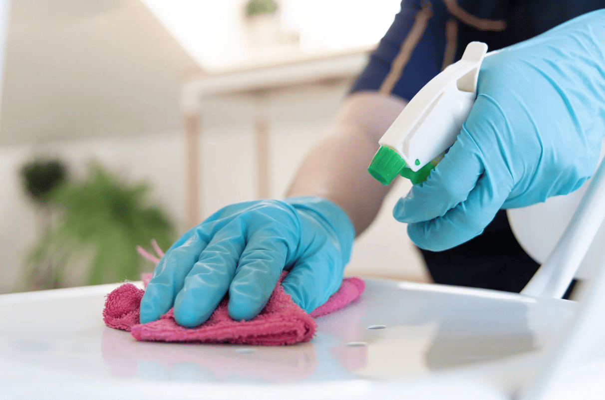 Woman's hands cleaning a worktop in rubber gloves with spray and a dish cloth.